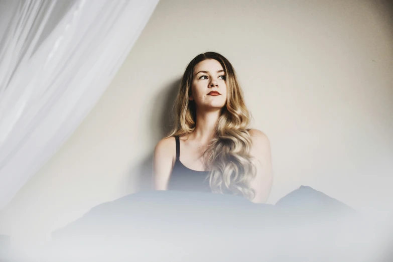 woman laying in bed with white sheer curtains