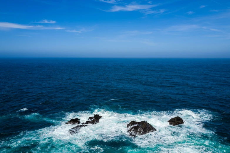 two rocks sit in the water and are being splashed by a boat