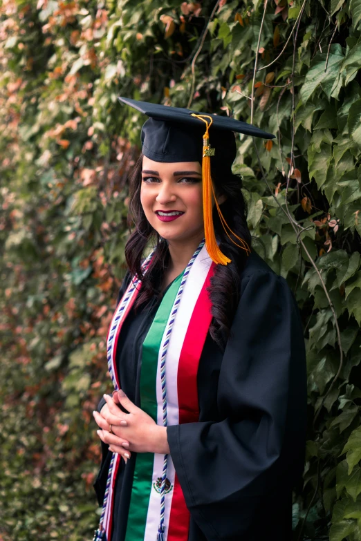 a beautiful young woman in a graduation gown standing in front of some trees