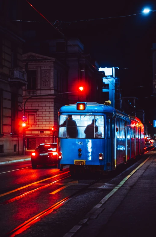 the blue train is traveling down the street at night