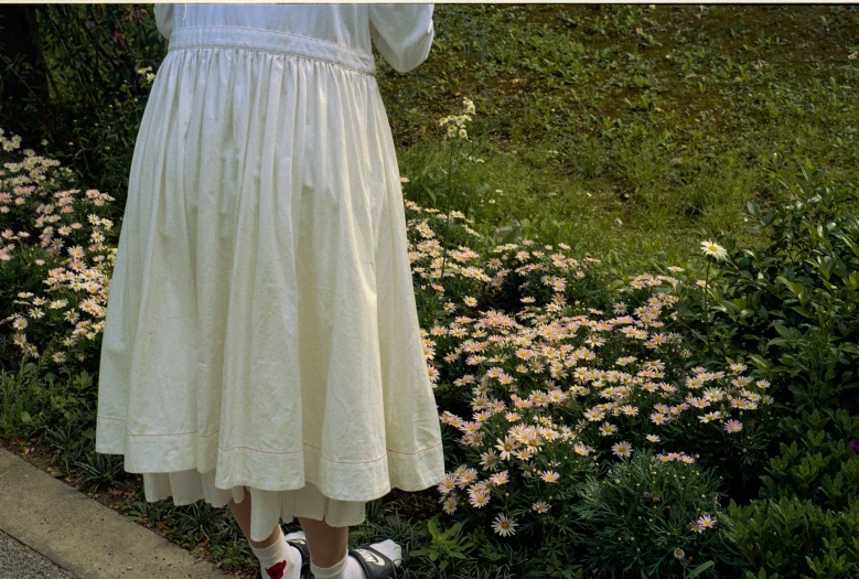 a woman wearing white dress by flowers, standing up