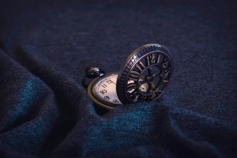 a black and gold pocket watch is on a dark cloth