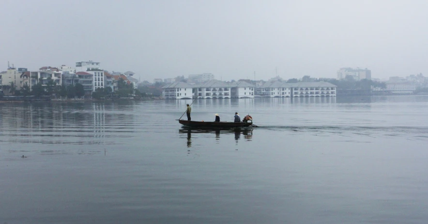 two people in a rowboat paddling in the water with buildings in the distance