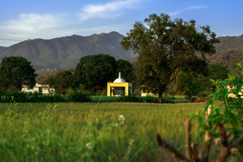 a field with a yellow house and mountains in the background