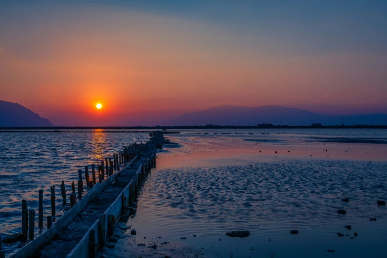 a pier in the water at sunset with an orange sky