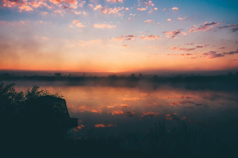 the sun setting over the water on a foggy day