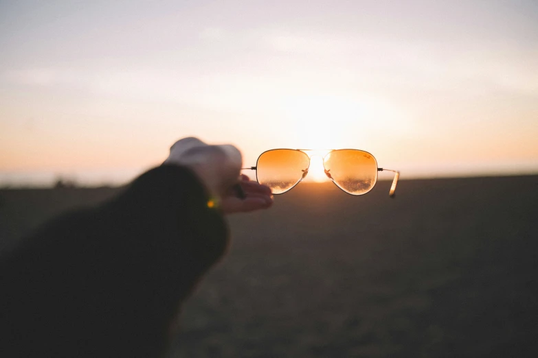 a hand holding onto sunglasses in the sky