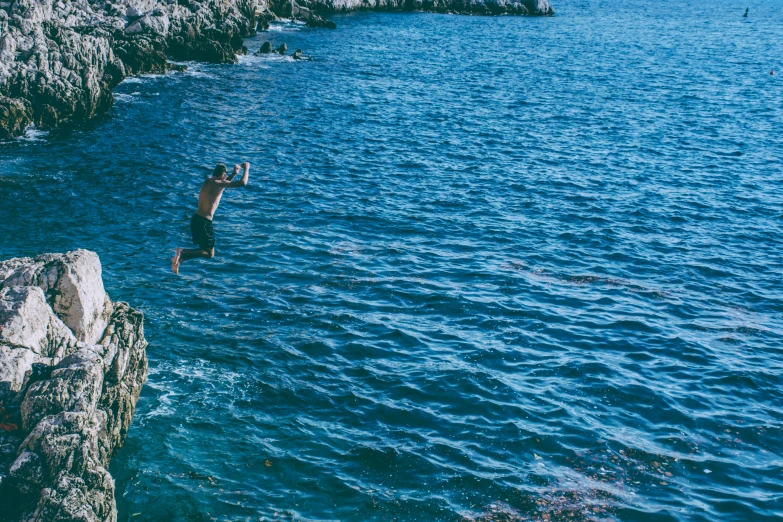 a man jumps into the water from cliffs to an ocean