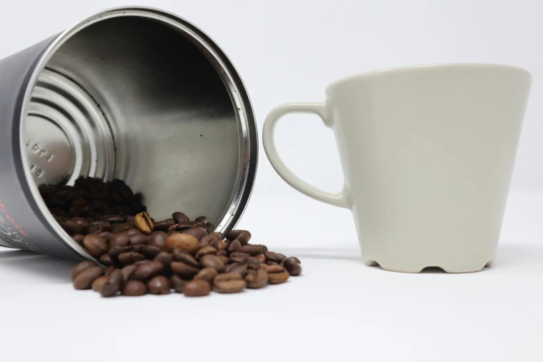 a white cup that is next to a can with some coffee beans