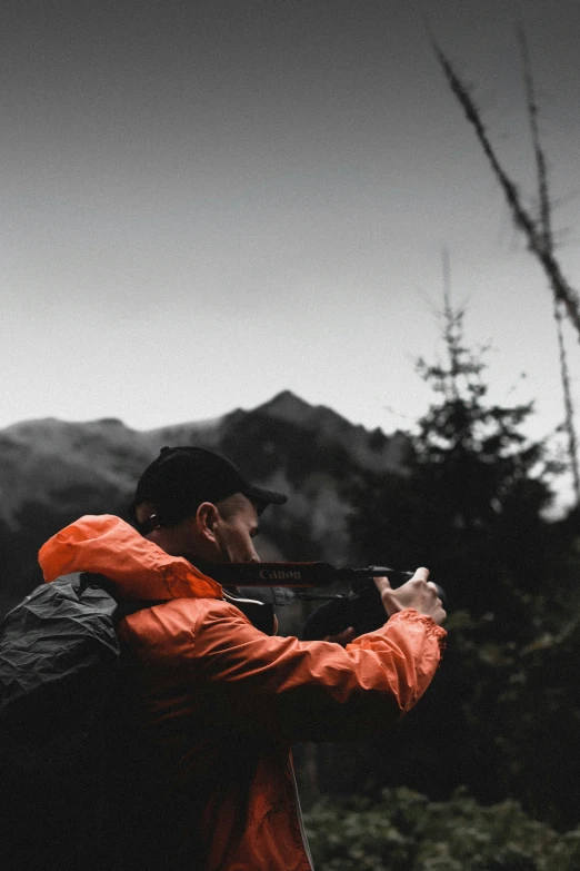 a man wearing an orange jacket shooting a rifle in the distance