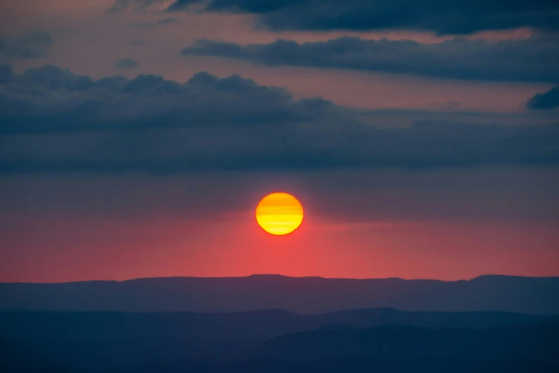 a sun is setting over some hills in the sky