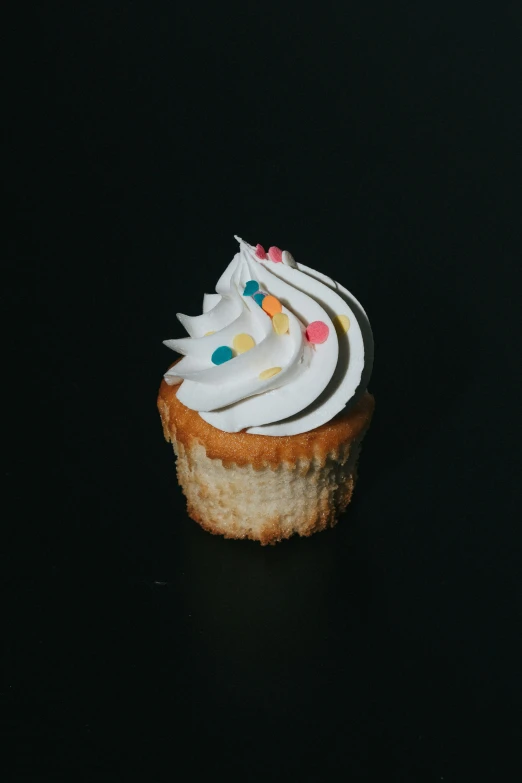 a cupcake with white frosting and multi - colored dots