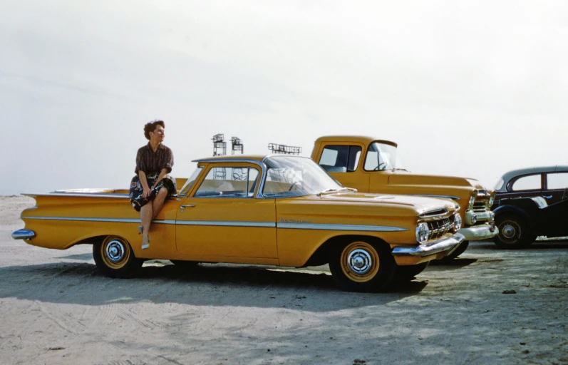 the woman is sitting on top of a vintage yellow car