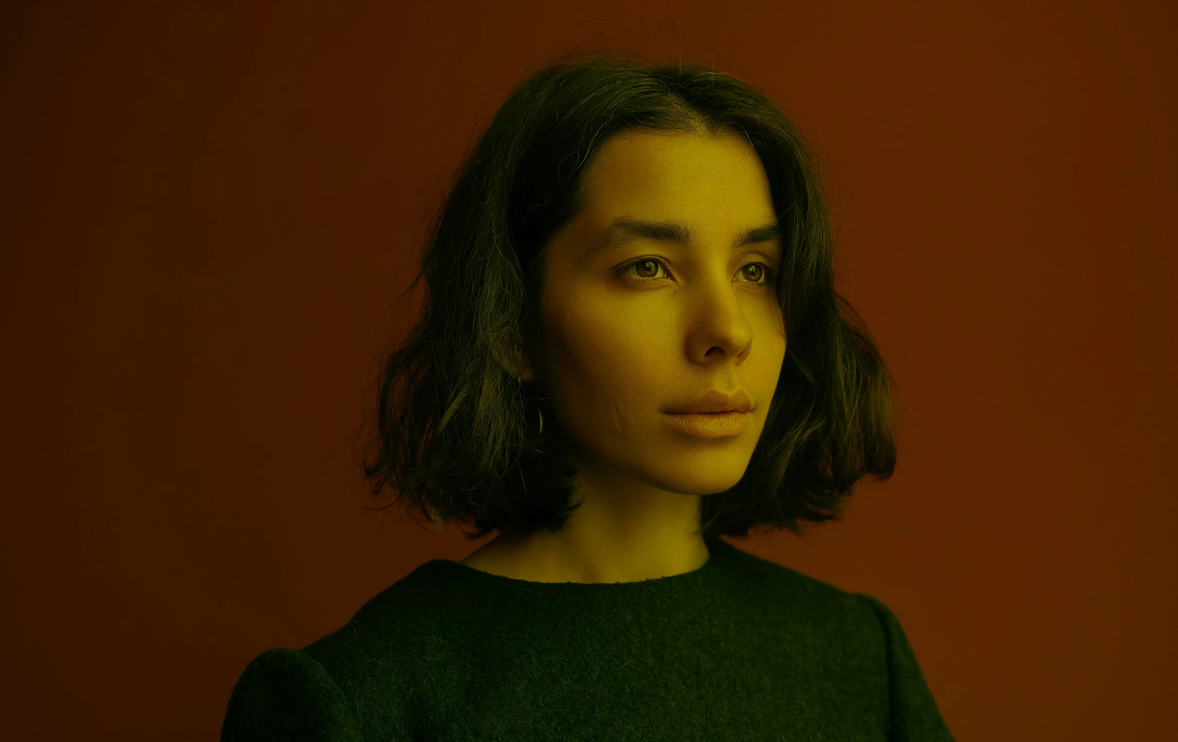 a woman with dark hair and green shirt is standing against a wall