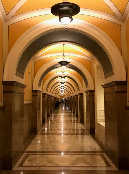 a long hallway with ceiling lights, a marble floor and columns