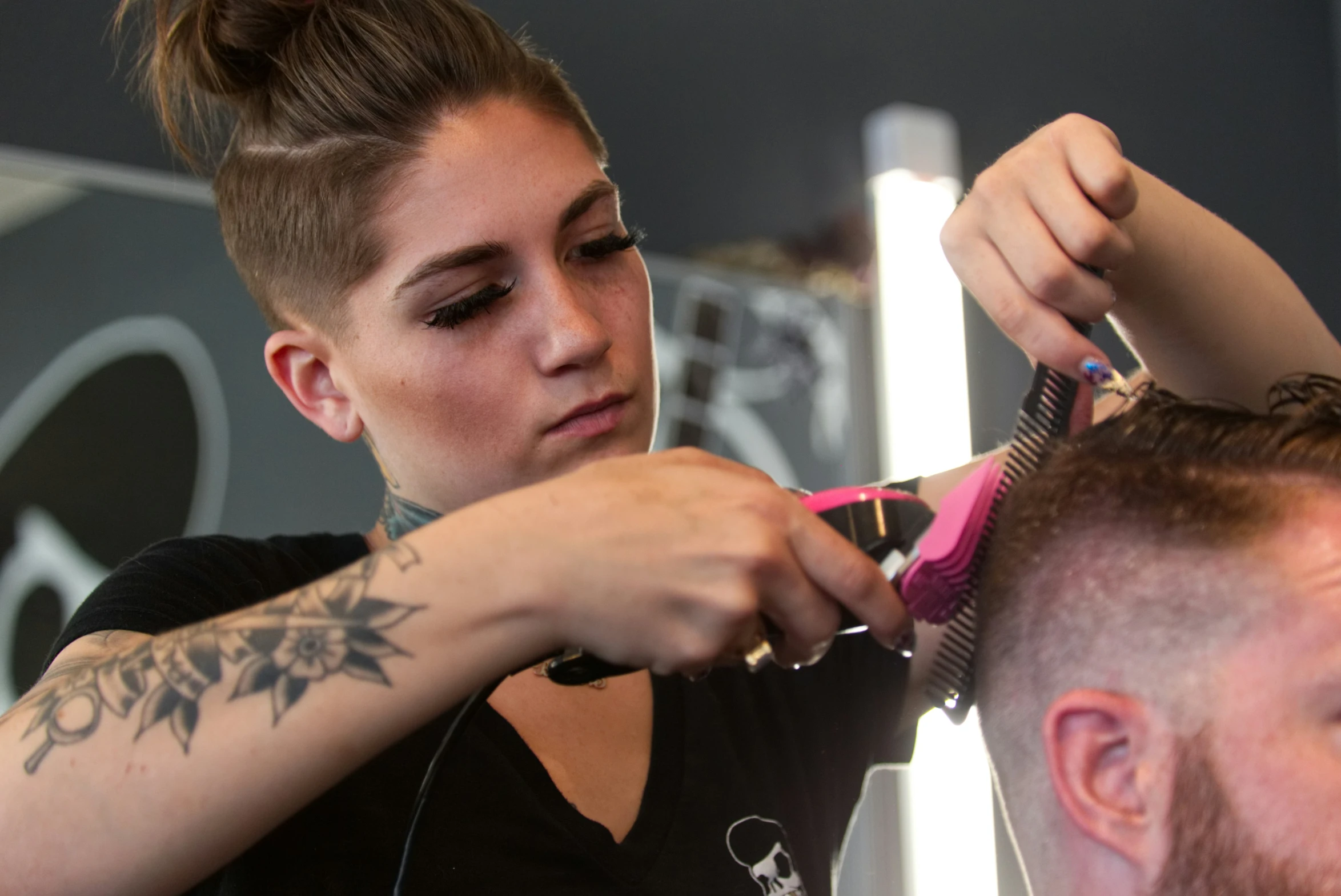 a female is having her hair styled by a male in the mirror