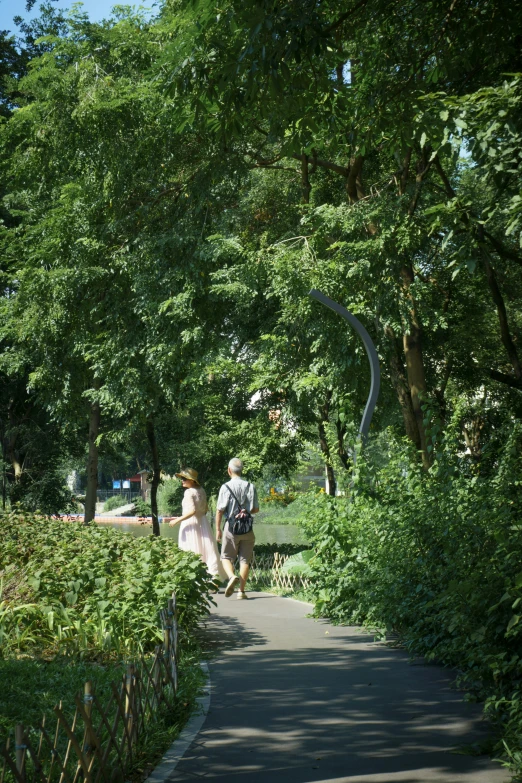 a man and a woman walking down a sidewalk through a park