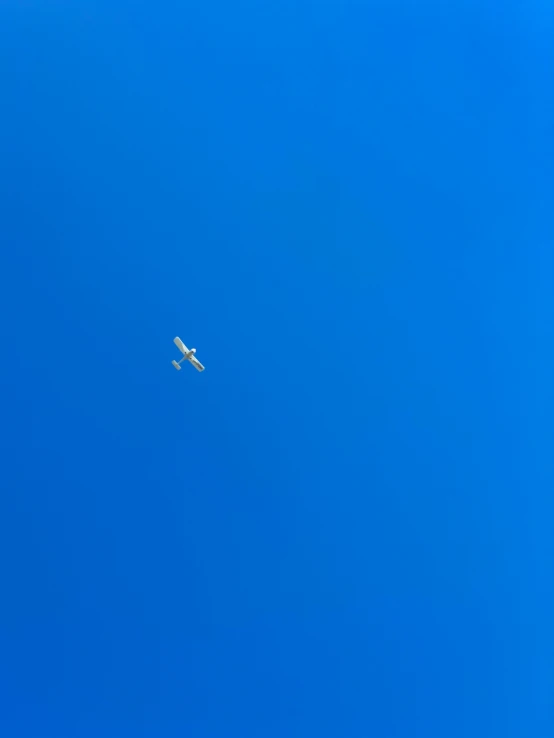 the small white airplane is flying in the blue sky