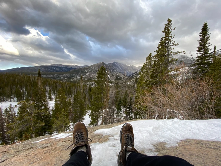 a person is sitting on top of the mountain while taking a picture of a forest