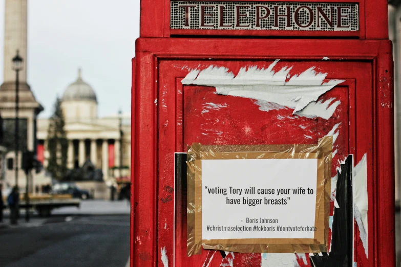 a sign on a red phone booth with a street in the background