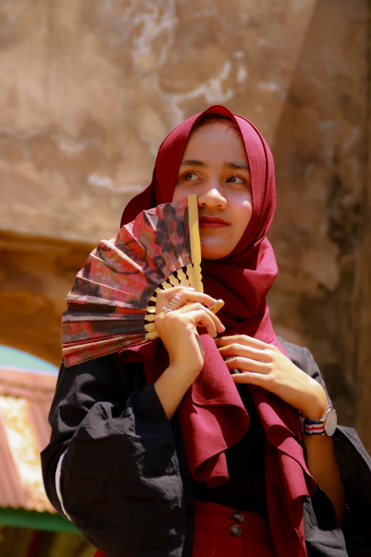 a young woman with a red shawl on holding up a fan