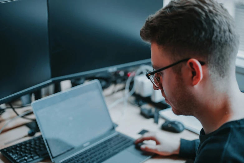 the man uses his laptop and monitor on the desk