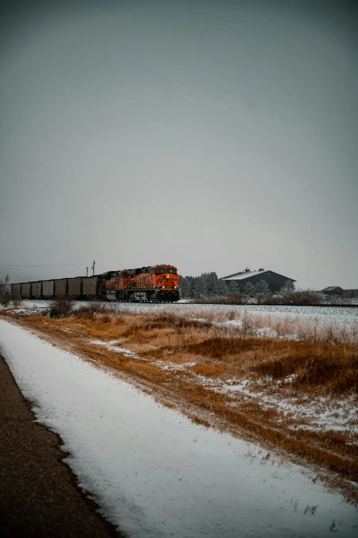 an orange and black train traveling past snow covered fields