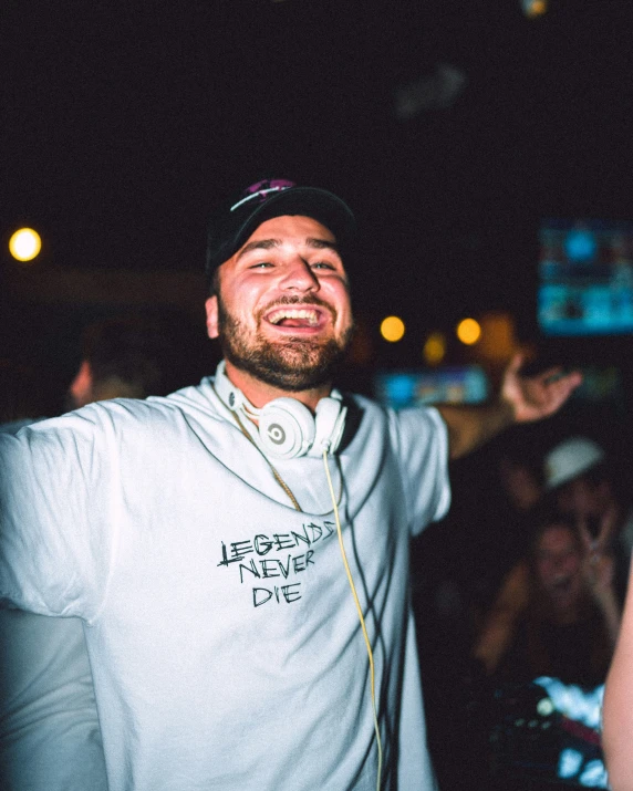 a man wearing ear buds, a white sweatshirt, and a hat standing in a crowd