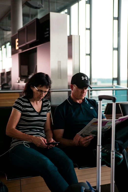 a man and woman sit on a bench reading a newspaper