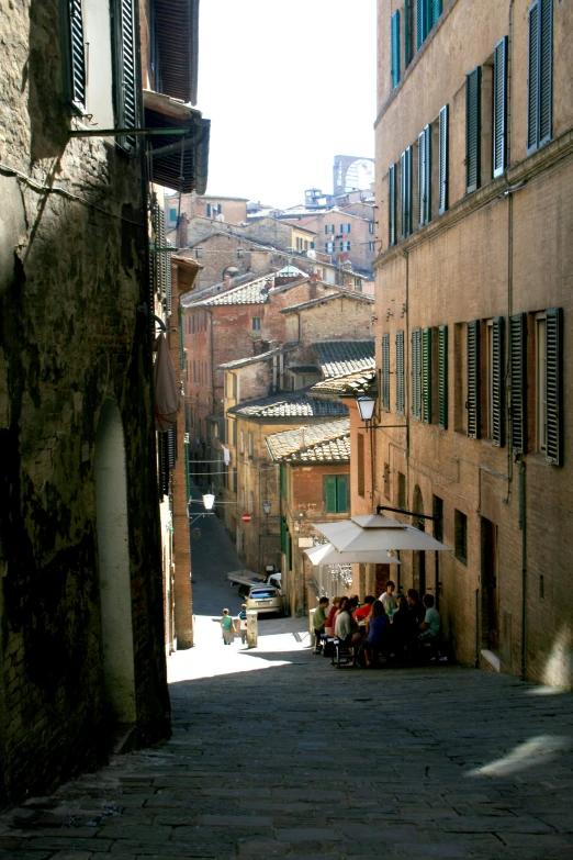 an old alley with people sitting under umbrellas