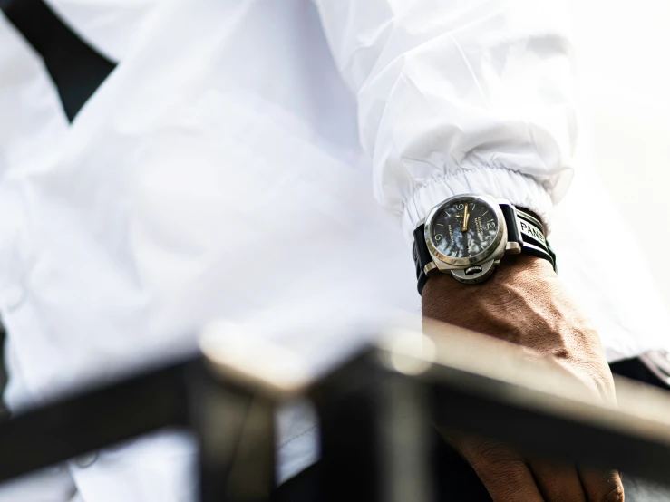 a man's wrist wearing a watch with his hands on a bench