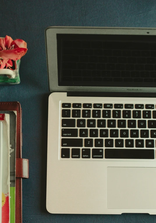 laptop computer on table next to water, flower and wallet