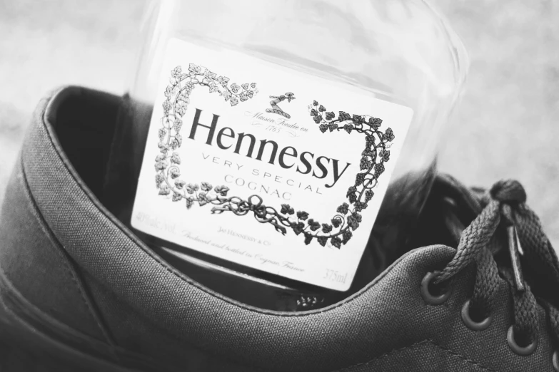 a glass jar with hennesy labels in it sits inside a pair of sneakers