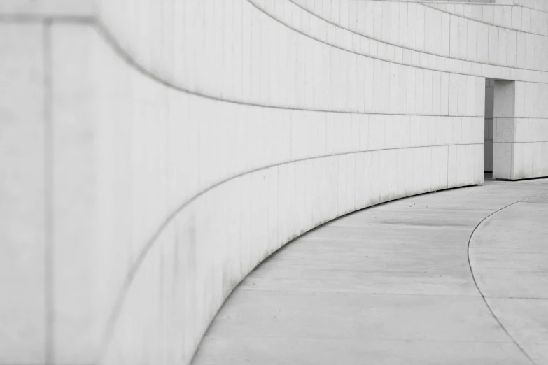 a black and white pograph of a concrete wall with a bench at the end