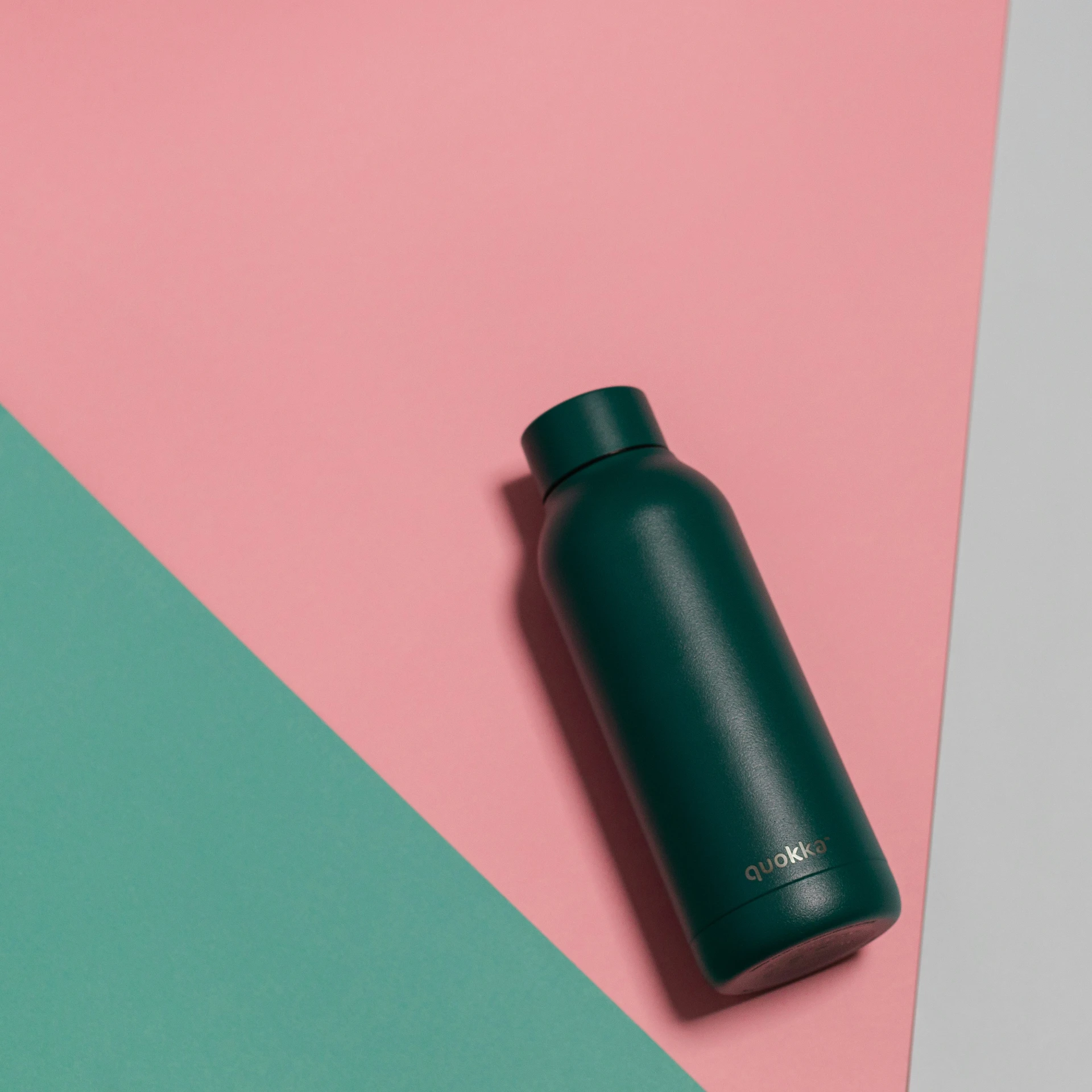 a teal green metal vacuum flask resting on a multi - colored surface