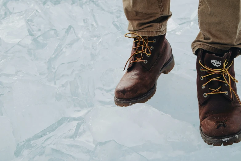 someone wearing brown boots standing on some ice