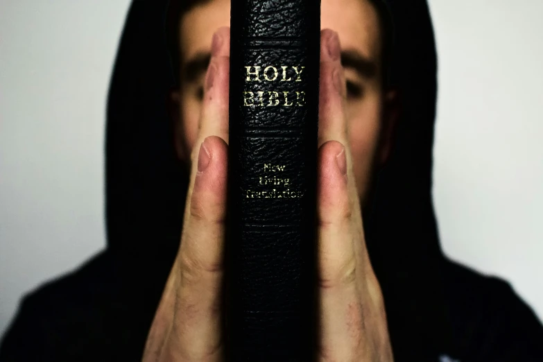 a man with black hair and dark hoodie holding his face up to the camera