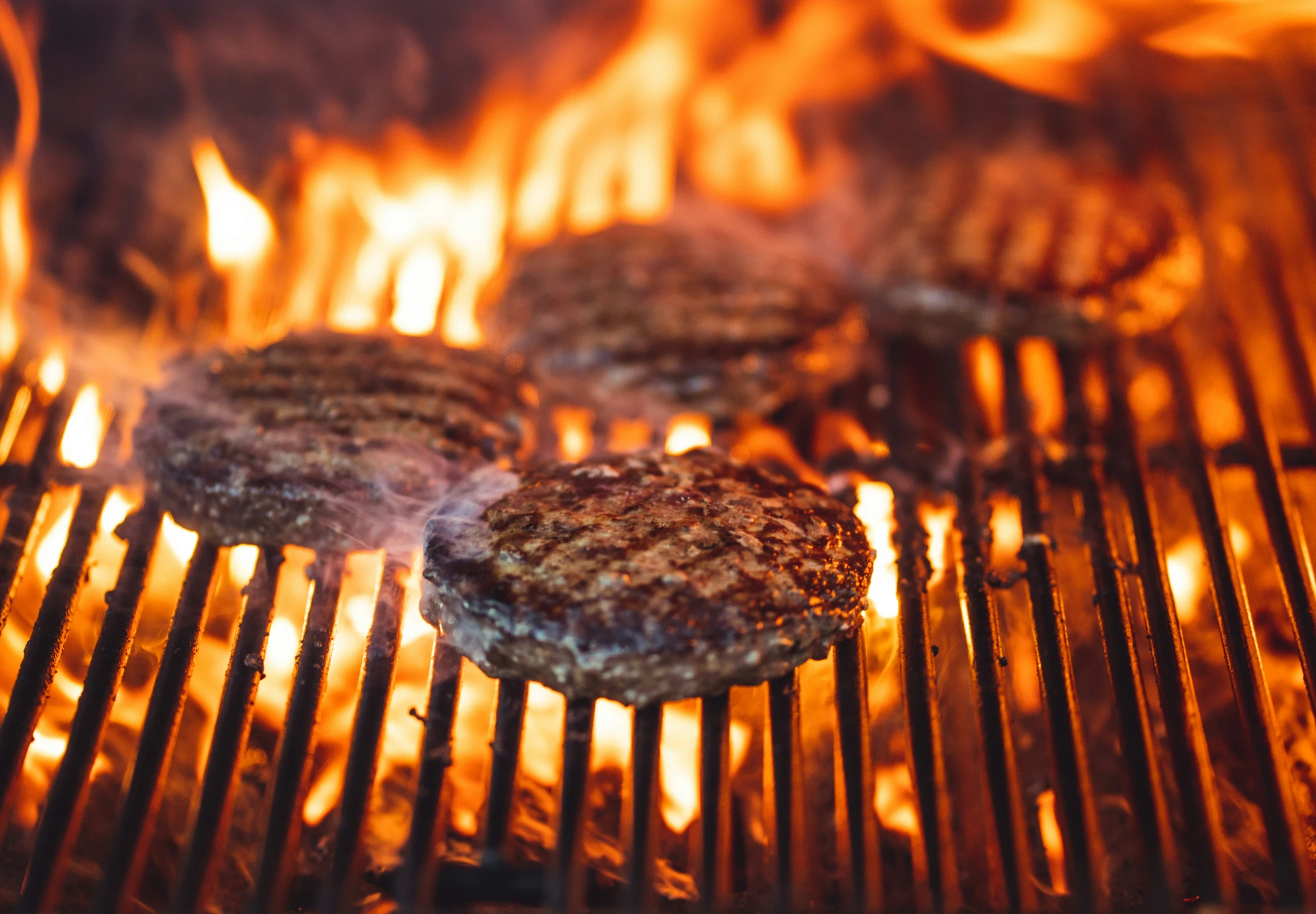 hamburger patties cooking on a grill over  coals