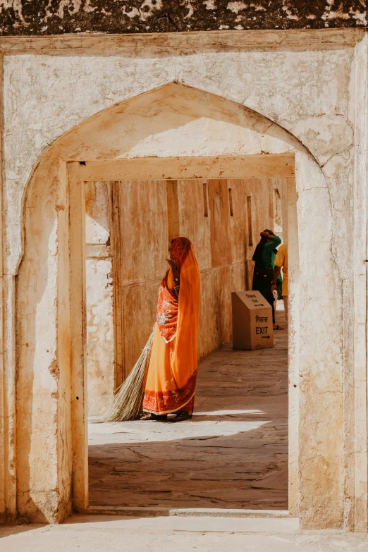 a woman in a bright orange sari walks past a building archway