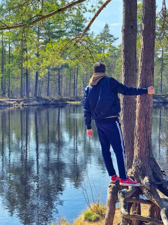 man standing on a log next to a lake