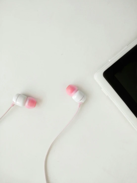 there are two white and pink ear buds next to an open tablet