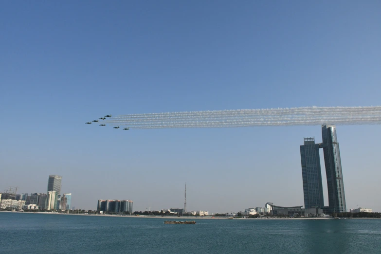 jets fly over the ocean with some buildings in the background