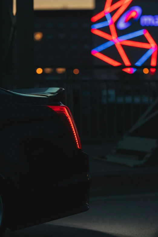 a black car is parked in the dark by a neon sign