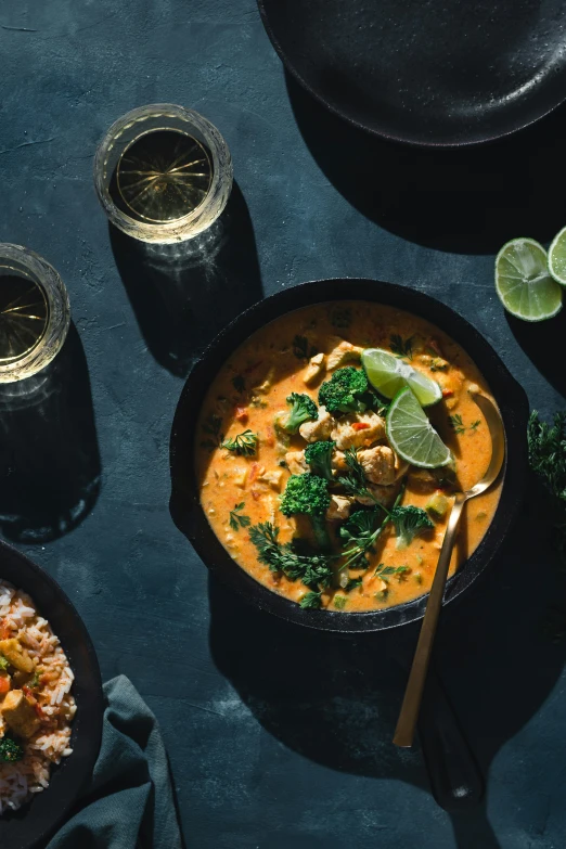 a bowl of soup with lime wedges and two bowls of other food