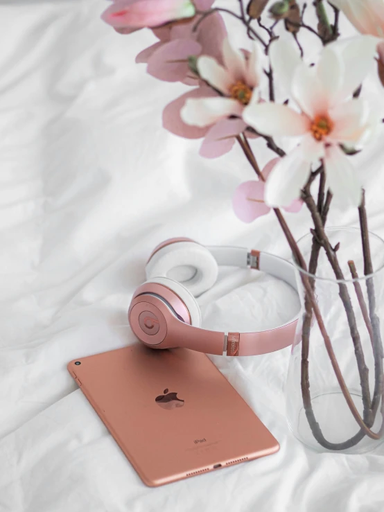 there are headphones and a pink apple device on a white sheet