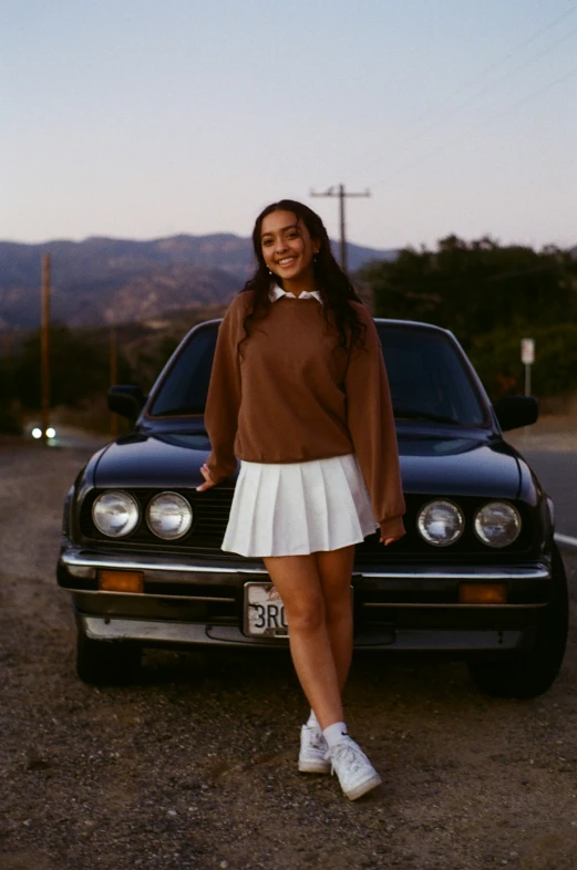 a girl in an old fashion dress standing in front of a black mustang