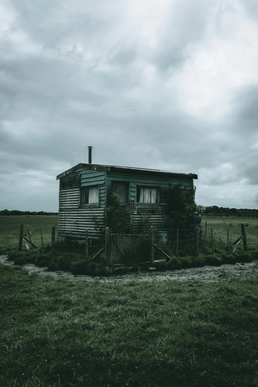 a abandoned cabin sits in the middle of a field on an overcast day