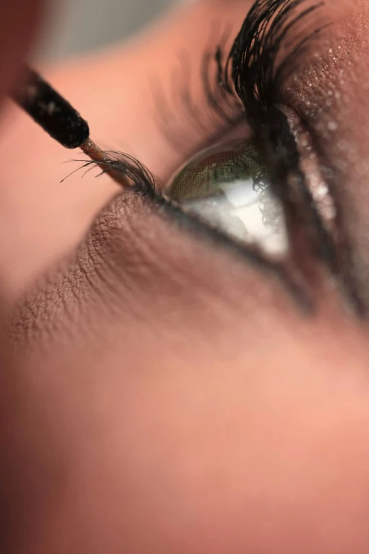 a eye with a black cat's eyeliner in the foreground, while someone holds a pen inside the eye and uses an eyewasher to brush its wrinkles