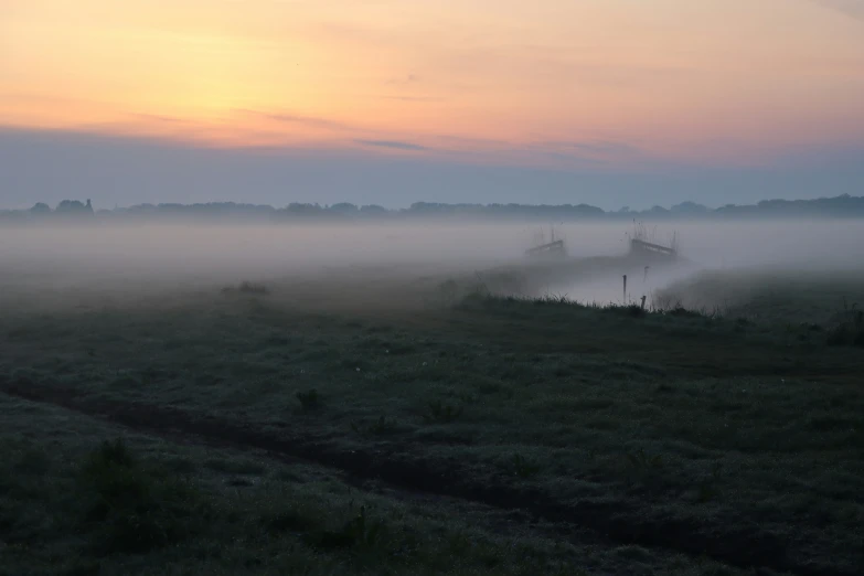 the fog is rolling on a farm field in front of the sun