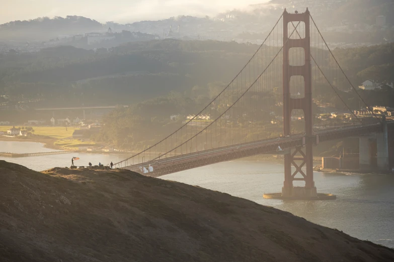 some people are on a hill by a suspension bridge